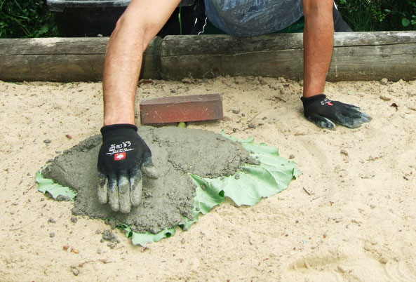 Vogeltränke aus Rhababerblatt herstellen - Betonmischung mit Maurerkelle und Arbeitshandschuhen auftragen